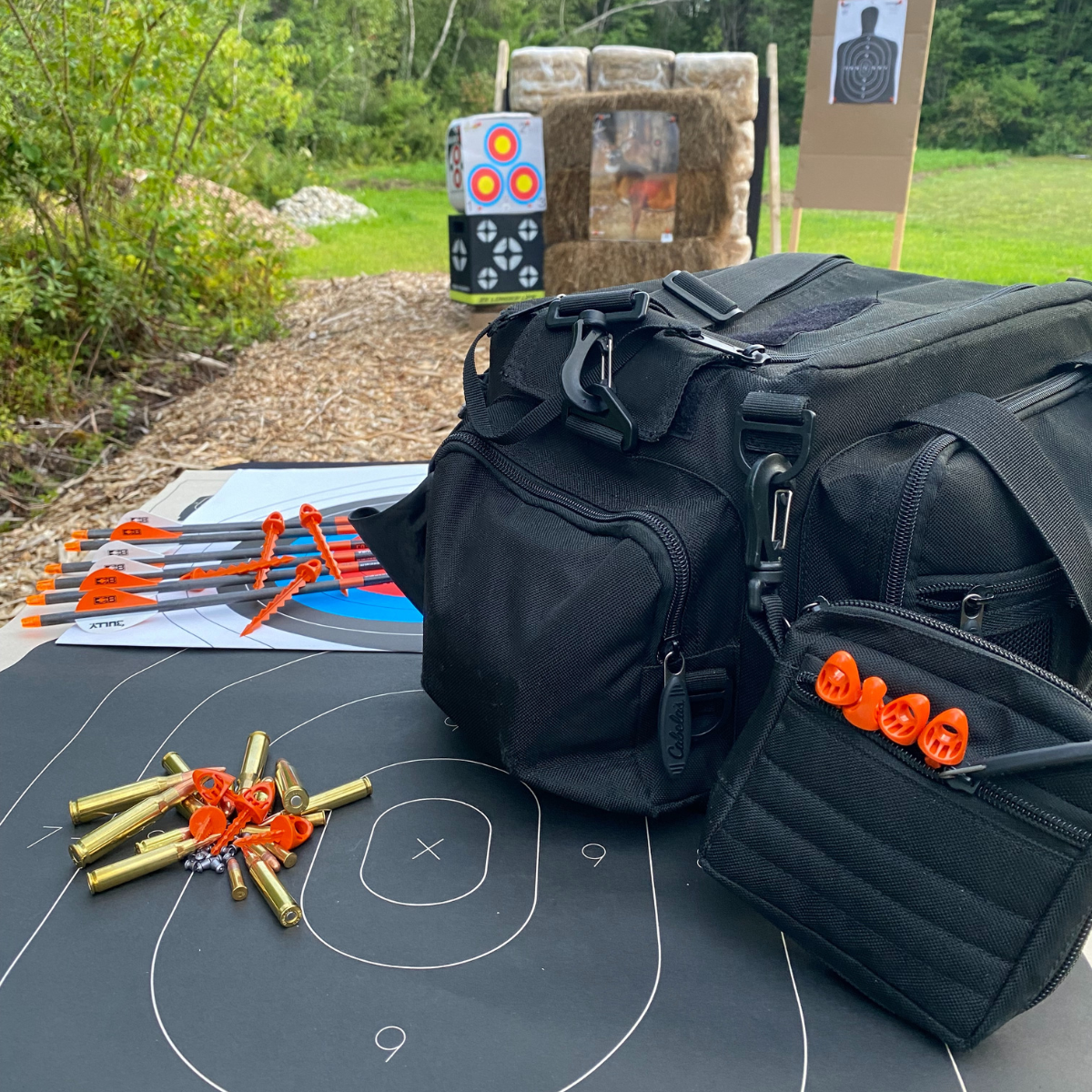 TargetTack Showcase - Black range bag with TargetTacks in pocket. The bag is sitting on a tabel with paper targets laid out on it, topped with ammo, crossbow bolts, and TargetTacks spread.