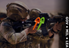 Soldier in camouflage gear holding a rifle overlayed with green and orange 1-inch TargetTacks, blurred background