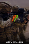 Person in military gear holding a weapon overlayed with orange and green 1-inch TargetTacks, blurred background