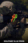 Person in military gear holding a rifle with colorful keychains, blurred background